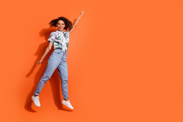 Full body photo of american woman in jeans and summer stylish shirt jumping overjoyed superhero isolated on orange color background