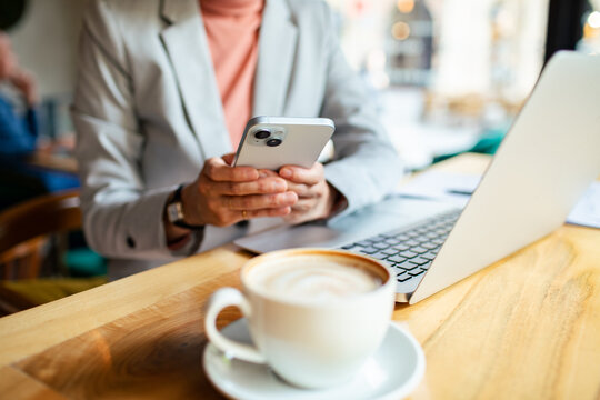 Businesswoman using smartphone and laptop while enjoying coffee in a cafe
