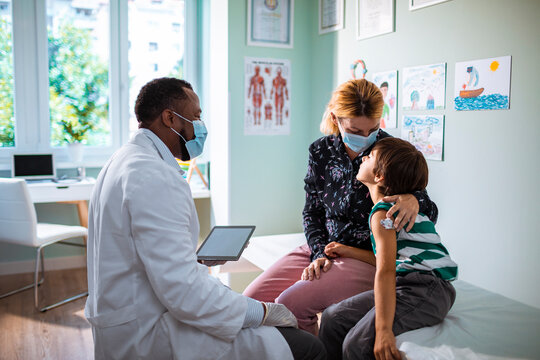 Pediatric doctor consulting with young boy and his mother in clinic