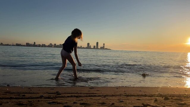 A child doing cartwheel on beach at sunset, with city skyline in the background