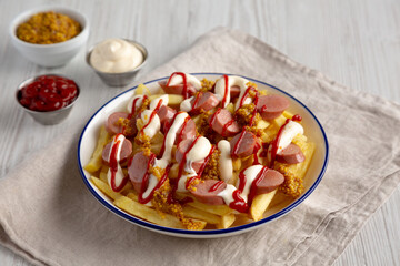 Homemade Salchipapa Fries with Ketchup, Mustard and Mayo on a Plate, side view.