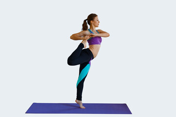 Beautiful fitness girl doing warm-up and stretching her legs on a light background