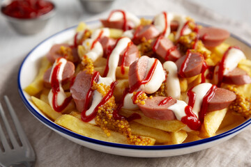 Homemade Salchipapa Fries with Ketchup, Mustard and Mayo on a Plate, low angle view. Close-up.
