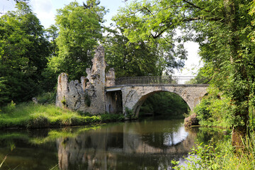 an ancient stone bridge and ruins over a tranquil river, surrounded by lush green trees. The scene combines historical charm with natural beauty, evoking a peaceful ambiance.