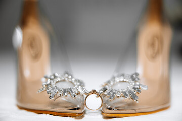 Two pairs of high heels with a ring on the left one. The shoes are made of gold and have a diamond-like design