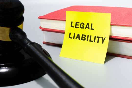 Judge's gavel with text legal liability on yellow note and red books.