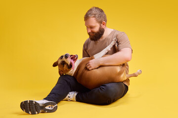 Young man posing lying on floor and plays with his lovely, relaxed American Staffordshire Terrier...