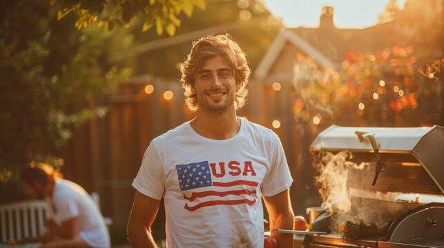 A young smiling American man with an American flag t-shirt stands on the back door of his house near a barbecue, the concept of celebrating independence day in America on the 4th of July with friends