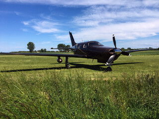 A small propeller plane stands on the grass of the airport