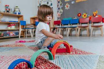 Little boy playing with rainbow wooden toy sitting on the floor in kindergarten