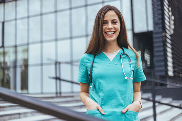 A joyful Caucasian female nurse poses outdoors, sporting a teal scrub with a stethoscope around her...