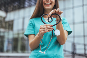 A smiling Caucasian female healthcare professional displays a stethoscope twisted into a heart...