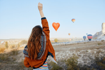 Woman gazing at colorful hot air balloons in the sky with arms raised in excitement