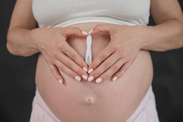 Caucasian woman holding a positive express pregnancy test against the background of her tummy. 