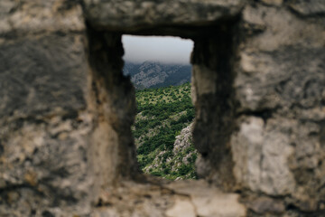 Old Bar medieval fortress in Montenegro. Stari Bar - ruined medieval city on Adriatic coast, Unesco World Heritage Site. A small defensive window in the wall overlooking the green mountains and hills.