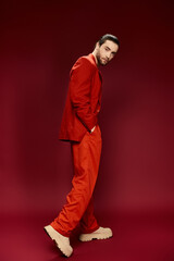 A stylish man with a red suit and no shirt striking a pose in a studio setting.