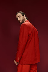 A dashing man in a striking red suit strikes a bold pose against a vibrant red backdrop in the studio.