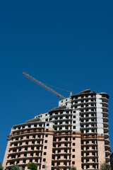 Fototapeta premium Construction of a multi-storey residential building with a crane on a background of blue sky