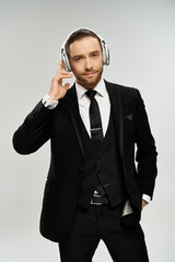 A bearded businessman in a stylish suit enjoying music with headphones on against a grey studio background.