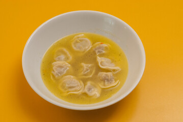 boiled dumplings with broth in a white bowl on a yellow background