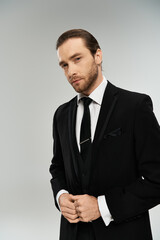 A charismatic, bearded businessman in a sharp suit and tie strikes a confident pose on a grey studio background.
