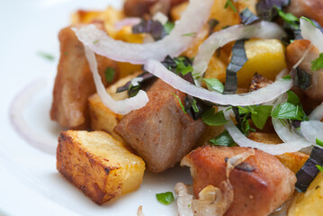 Fried meat with potatoes, onion and herbs on a white plate