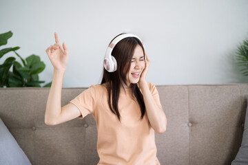 Happy Young Asian woman wearing headphone have fun and dancing listening to music relax in living...
