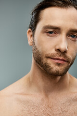 Obraz premium Handsome shirtless man with a beard striking a pose on a grey background in a studio setting.