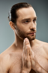 Fototapeta premium A shirtless, bearded man stands with his hands together, exuding a sense of peace and contemplation in a studio setting.