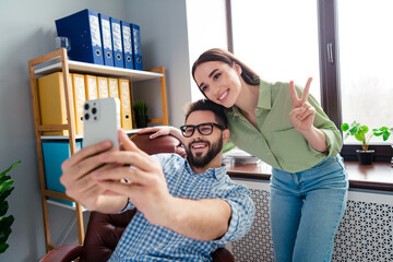 Photo of two people sit chair in workplace workstation make selfie girl show v sign