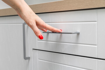 housewife opens a kitchen cabinet drawer with her hand, close-up