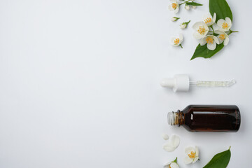 Aroma oil bottle arranged with jasmine flowers on a white background. Flower essential oil. Herbs have medicinal properties. Top view, flat lay. Space for text.