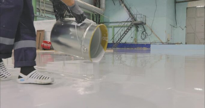 A builder pours polymer flooring material onto the prepared surface. A builder pours construction material for polymer floors onto the floor