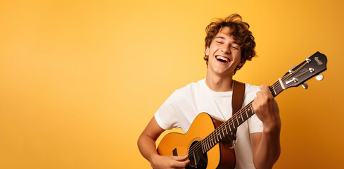 Naklejka premium Happy teenage boy playing guitar on yellow background. Place for text
