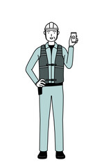 Senior male engineer in helmet and work wear using a smartphone at work.