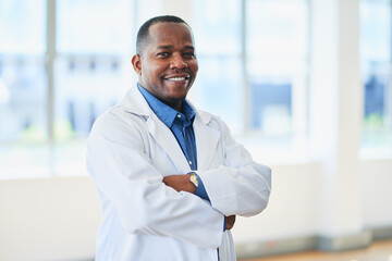 Confident Black Doctor in White Coat Standing with Arms Crossed in Bright Clinic