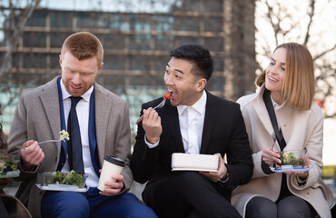 Front view of three multiethnic business colleagues eating outdoors healthy home made salads