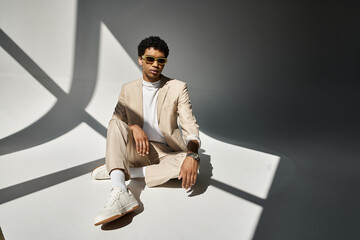 African American man in beige suit sitting comfortably on the floor, wearing stylish sunglasses.