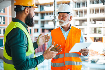 A diverse construction worker converses with a senior site manager at a bustling building site,...