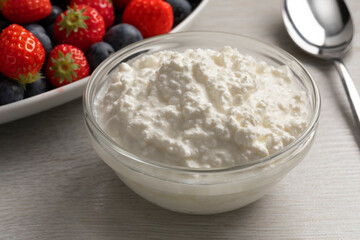 Glass bowl with cottage cheese close up and fresh fruit in the background 