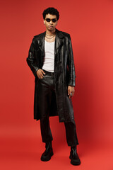 Handsome African American man in black leather coat posing against red background.