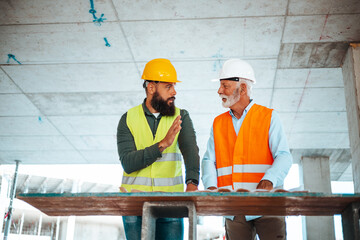 Two professional construction site managers in safety vests and helmets engage in a strategic...