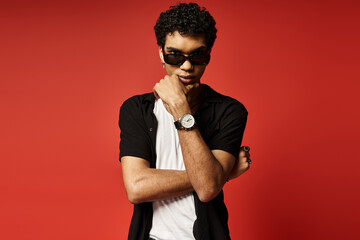 Young African American man with sunglasses striking a pose with watch against red backdrop.