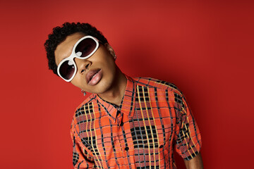 Handsome African American man in plaid shirt and sunglasses on vibrant red background.