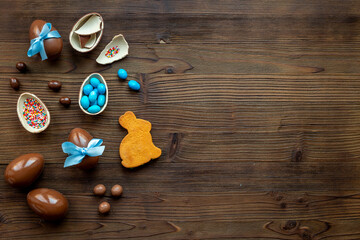 Chocolate Easter eggs in blue ribbon and bunny cookies on wooden background