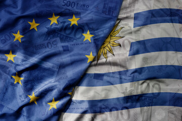 big waving realistic national colorful flag of european union and national flag of uruguay on a euro money banknotes background.