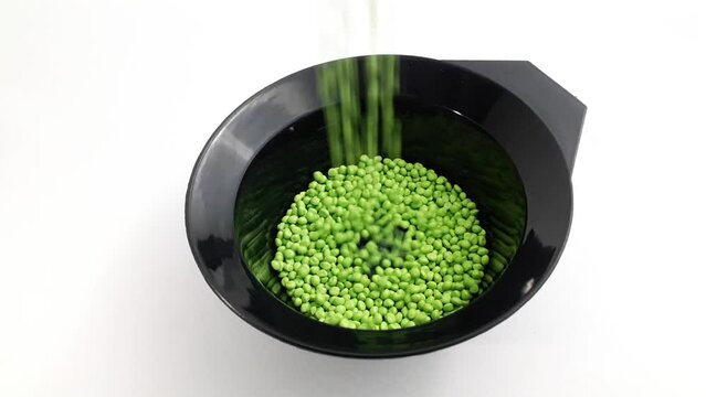 Light green masterbatch granules are poured into a black measuring cup on a white background, this polymer is a colorant for products in the plastics industry.