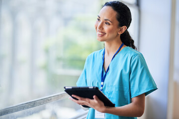 Smiling Nurse Standing by Window Holding Digital Tablet in Hospital