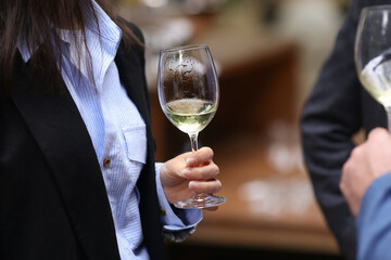 Shallow depth of field (selective focus) details with the hand of a woman holding a glass of white wine at a party.