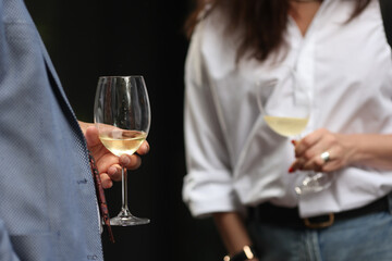 Shallow depth of field (selective focus) details with the hand of a man holding a glass of white wine at a party.